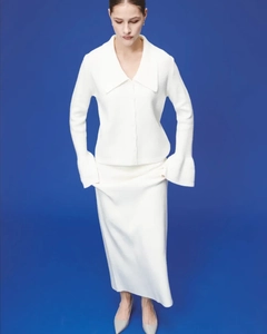 Detail of white knit cardigan and matching long skirt set on a model with blue background