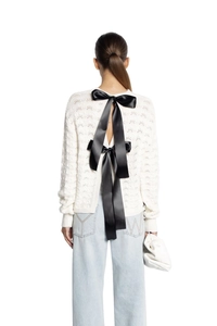 Close-up of elegant white open-back knit sweater with long black satin bow ties