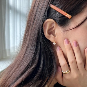Detail shot of a pearl earring, tricolor metal ring, and orange resin hair clip on a model