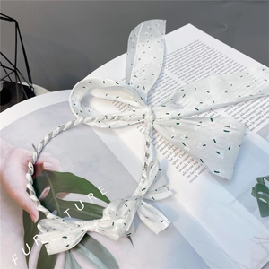 Detailed view of white fabric headband with green polka dots and elegant bow accents