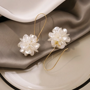 Macro shot of long white floral petal earrings with golden hooks on grey silk and ceramic