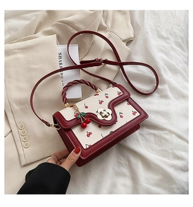 Detail of red cherry print shoulder bag with golden floral twist lock and charm