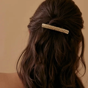 Detailed view of a golden hammered texture hair clip styled on dark brown curly hair