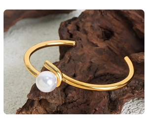 Detail view of a gold plated titanium steel open cuff bracelet with a white round pearl