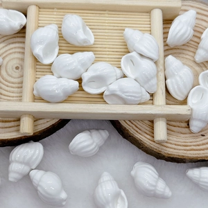 Detailed view of white shell-shaped ceramic beads for DIY jewelry on a wooden tray