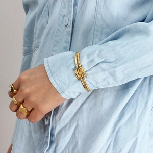 Detail of a gold knotted bracelet and rings set worn over a blue denim sleeve