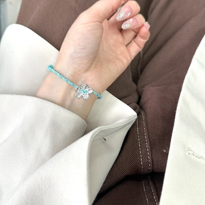 Detailed view of handmade blue braided bracelet with silver flower charm on a wrist