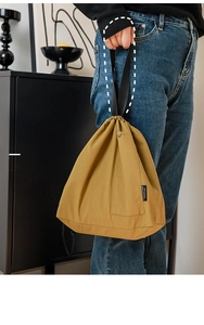 Detail of mustard yellow drawstring lunch bag showing handheld straps and side pocket