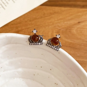 Macro detail of crown-shaped stud earrings with amber brown pearls on a ceramic bowl