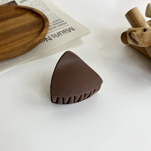 Detail of matte dark brown triangular hair claw clip on a minimalist aesthetic background