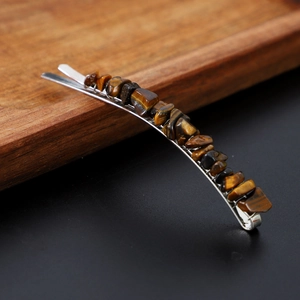 Detailed close-up of Tiger Eye crystals on a metal hair clip over a dark wood tray