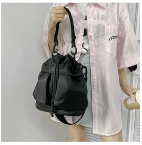 Detailed view of black nylon drawstring bucket bag with front utility pockets shown on model
