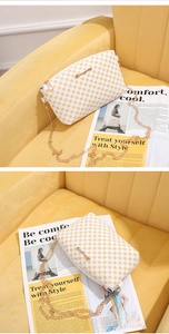 Close-up of white crossbody bag with yellow dots and gold chain on warm textile