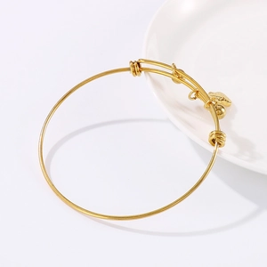 Adjustable golden stainless steel bracelet with a small heart charm on white porcelain