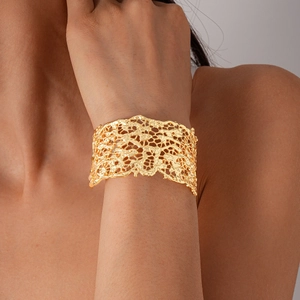 Close-up of a wide gold lace-textured open cuff bracelet worn on a model wrist