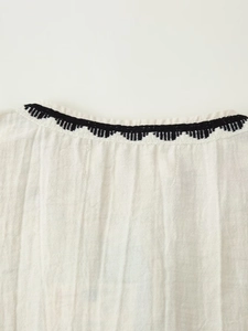 Detail of bohemian embroidery and linen fabric texture on an off-white summer vest