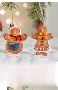 Close-up of cute resin gingerbread man and woman ornaments hanging on a green pine tree