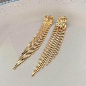 Detail view of long gold tassel earrings on a decorative plate with macro metallic texture