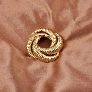 Detailed view of a gold woven texture feminist brooch on soft brown silk background