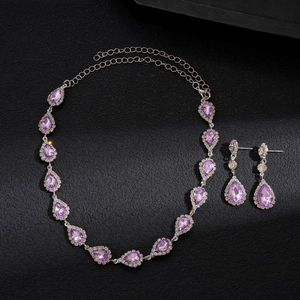 Close-up of purple teardrop pendant and earrings with pavé diamond halo on black surface