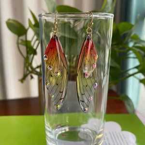 Detailed view of cicada wing earrings with red-yellow gradient and rainbow rhinestones