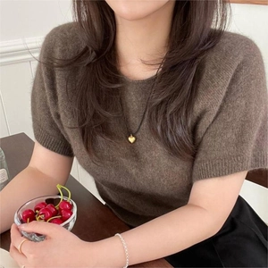 Detail of a gold heart pendant necklace on black cord styled with brown knit top