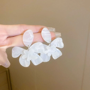 Close-up of white resin flower earring with marble texture held against a warm wall