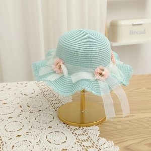 Détail d'un chapeau de paille bleu avec fleurs en tissu rose et bordure en dentelle blanche