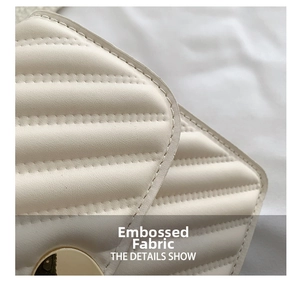 Detail showing the embossed fabric texture and gold circular metal lock on a cream bag