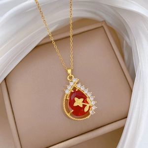 Close-up of gold teardrop necklace with red gemstone on beige jewelry box and white silk