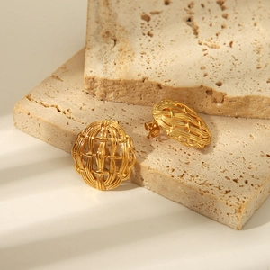 Détail de boucles d'oreilles ovales tissées dorées avec texture géométrique sur pierre