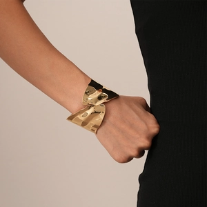 Detailed view of wide irregular golden metal cuff bracelet with fluid wavy design