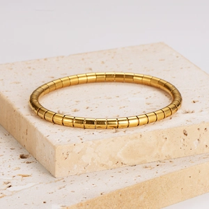 Minimalist gold bamboo joint snake bone bracelet displayed on a beige stone block