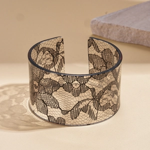 Detail view of a wide acrylic bangle with intricate black lace patterns and open cuff design