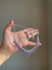 Macro detail of silver necklace and earrings set with purple teardrop gemstones and diamonds