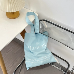 Detail of light blue canvas tote bag with Harmony print hanging on a transparent chair