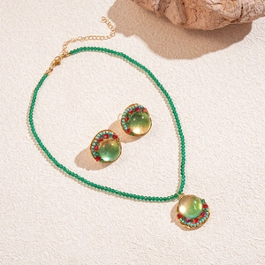Vintage resin beaded necklace and earrings set with green stones on a rock background