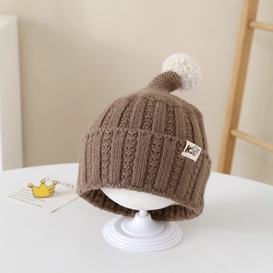 Detail of soft brown knit beanie featuring a white pom-pom and cute dog patch