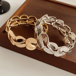 Detail of gold and silver S-shaped metal bracelets with a smooth finish on a wooden tray