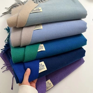 Detail of stacked solid color pashmina scarves in blue and purple with fringe and labels