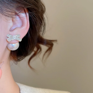 Detail view of silver bow stud earring with sparkling crystals and a large white pearl