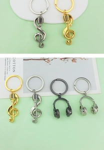 Detailed views of gold and silver music note charms and headphones keychains on green backdrop