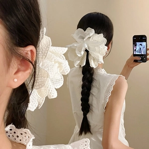 Detail showing oversized white lace flower hair clip with pearl center on braided hair
