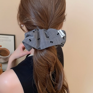 Détail d'un chouchou gris à rayures avec nœud et étiquette Happiness sur une queue de cheval
