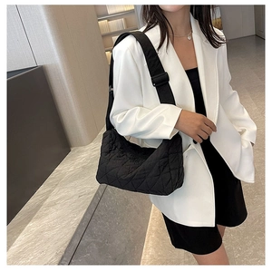 Close-up of black quilted crossbody bag with adjustable wide strap on white blazer