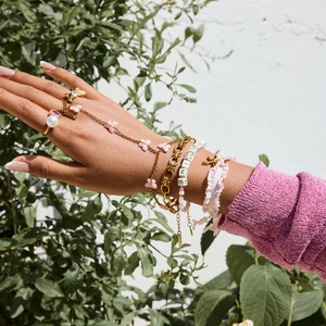 Detail of layered gold bracelet set with pink butterflies and SHINE letter beads