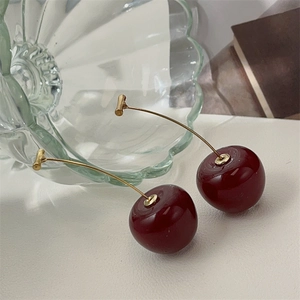 Macro detail of red cherry earrings with gold hooks placed on a vintage background