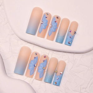 Faux ongles longs forme cercueil avec dégradé, motifs floraux bleus et strass brillants