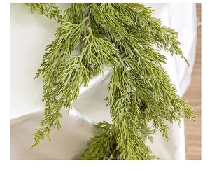 Close-up of lifelike green PE cedar garland needles against white satin fabric