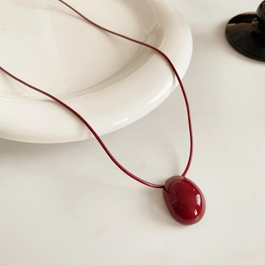 Vue détaillée d'un collier pendentif ovale bordeaux sur un plateau minimaliste